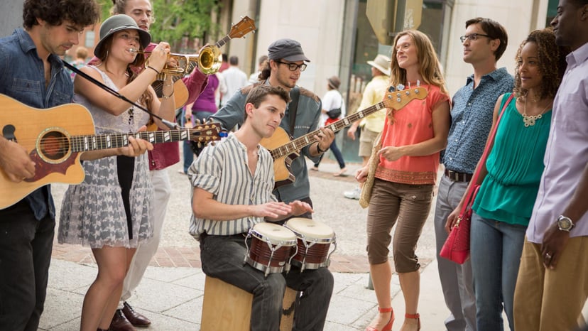 A busker sits amid other musicians and an audience playing the bongos in Asheville