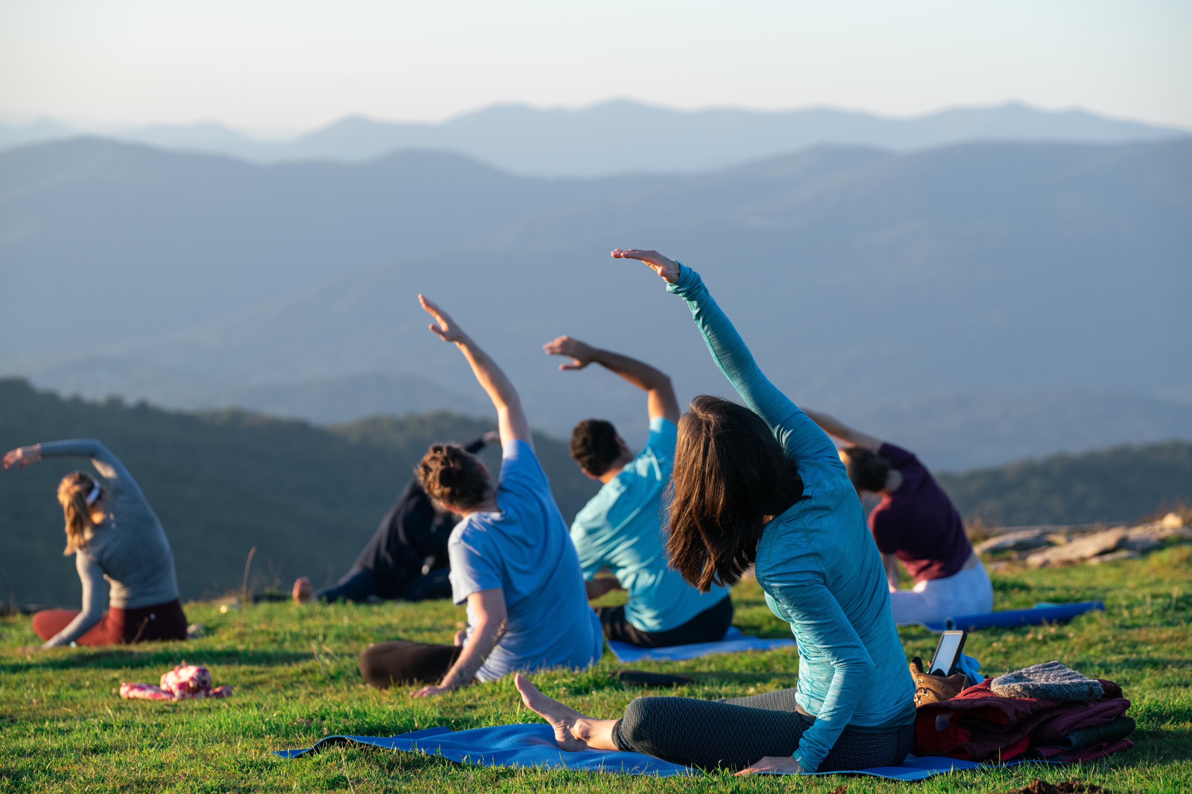 A view from behind of a group of people doing yoga in a green meadow in Asheville