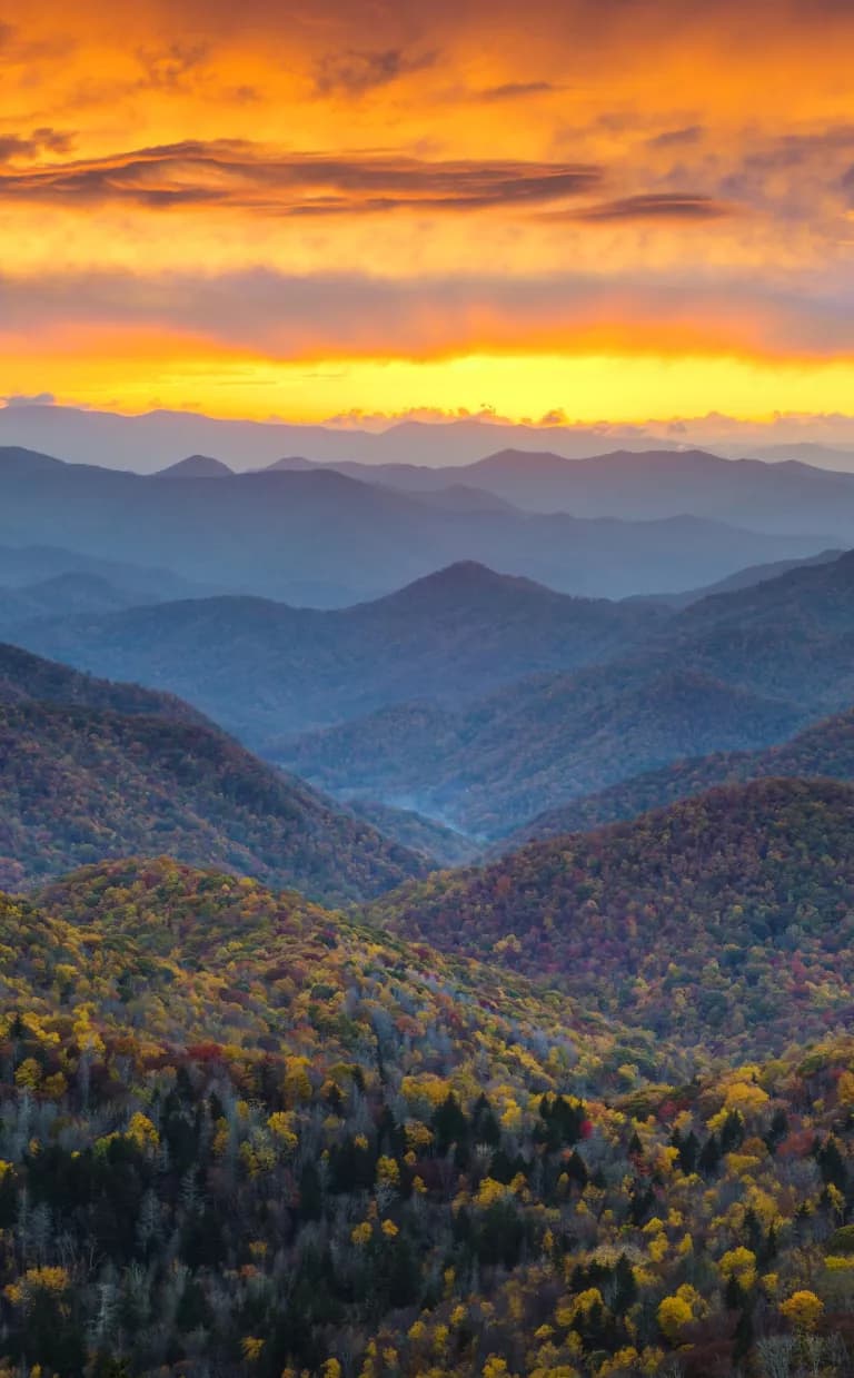 Blue mountains below a sun-streaked orange sky in Asheville