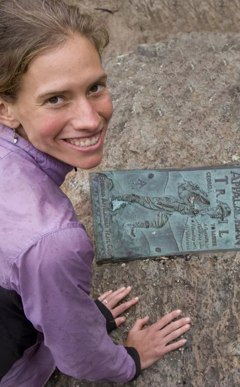 A hiker poses next to an Appalachian Trail plaque