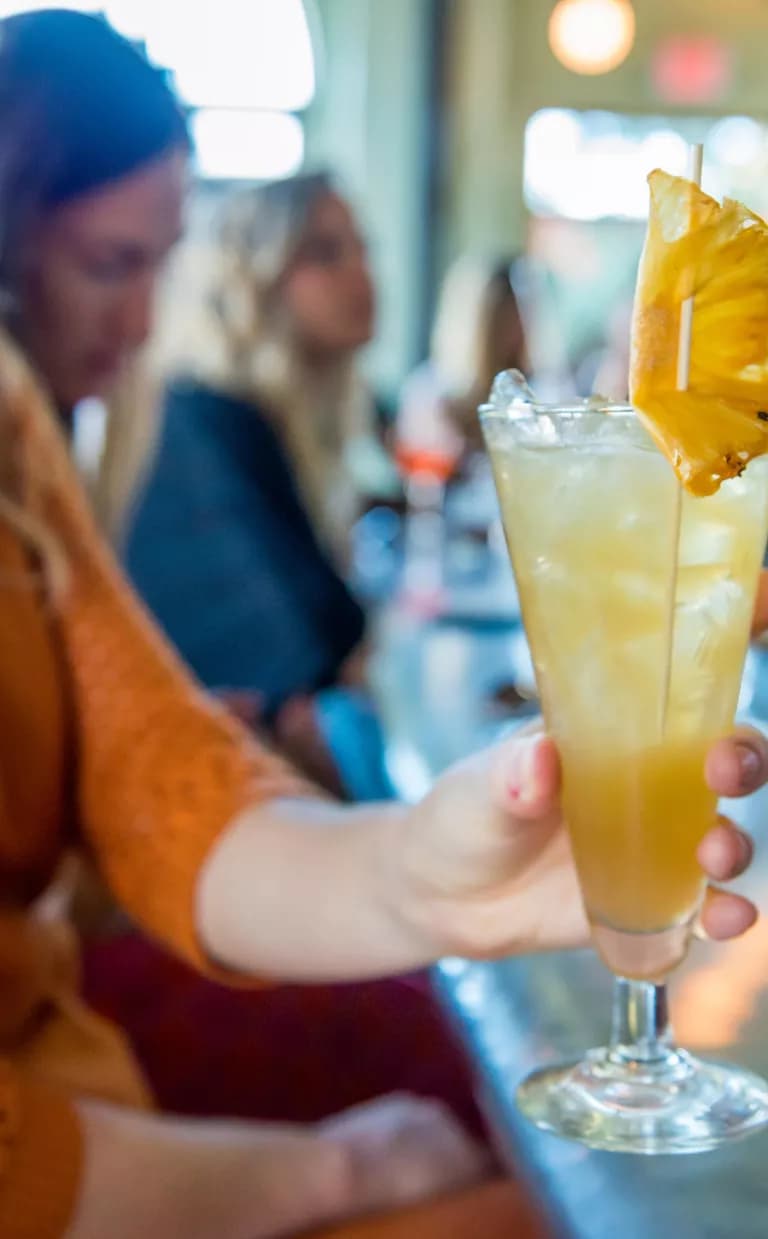 A person at a bar holds an orange-y cocktail up to the camera in Asheville