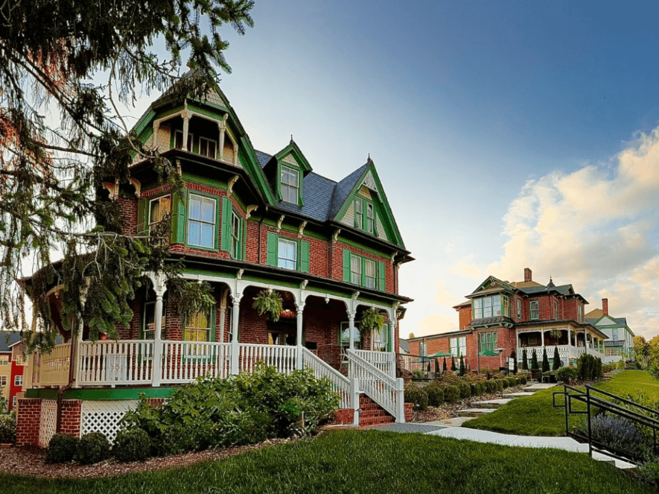 brick house with green trim and white wrap around porch with sunset in background brick house with green trim and white wrap around porch with sunset in background