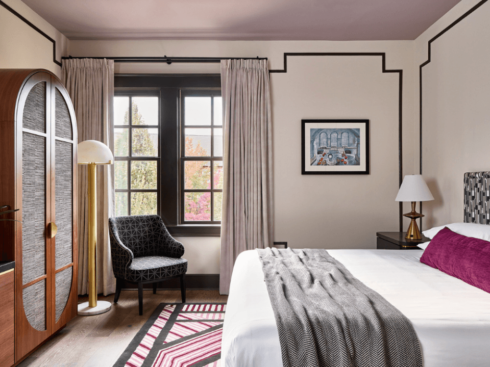 clean white room with brown oval armoire, white linen bed with purple pillow and grey throw blanket clean white room with brown oval armoire, white linen bed with purple pillow and grey throw blanket
